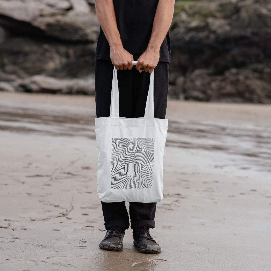 man holding white shopper tote bag with wave design