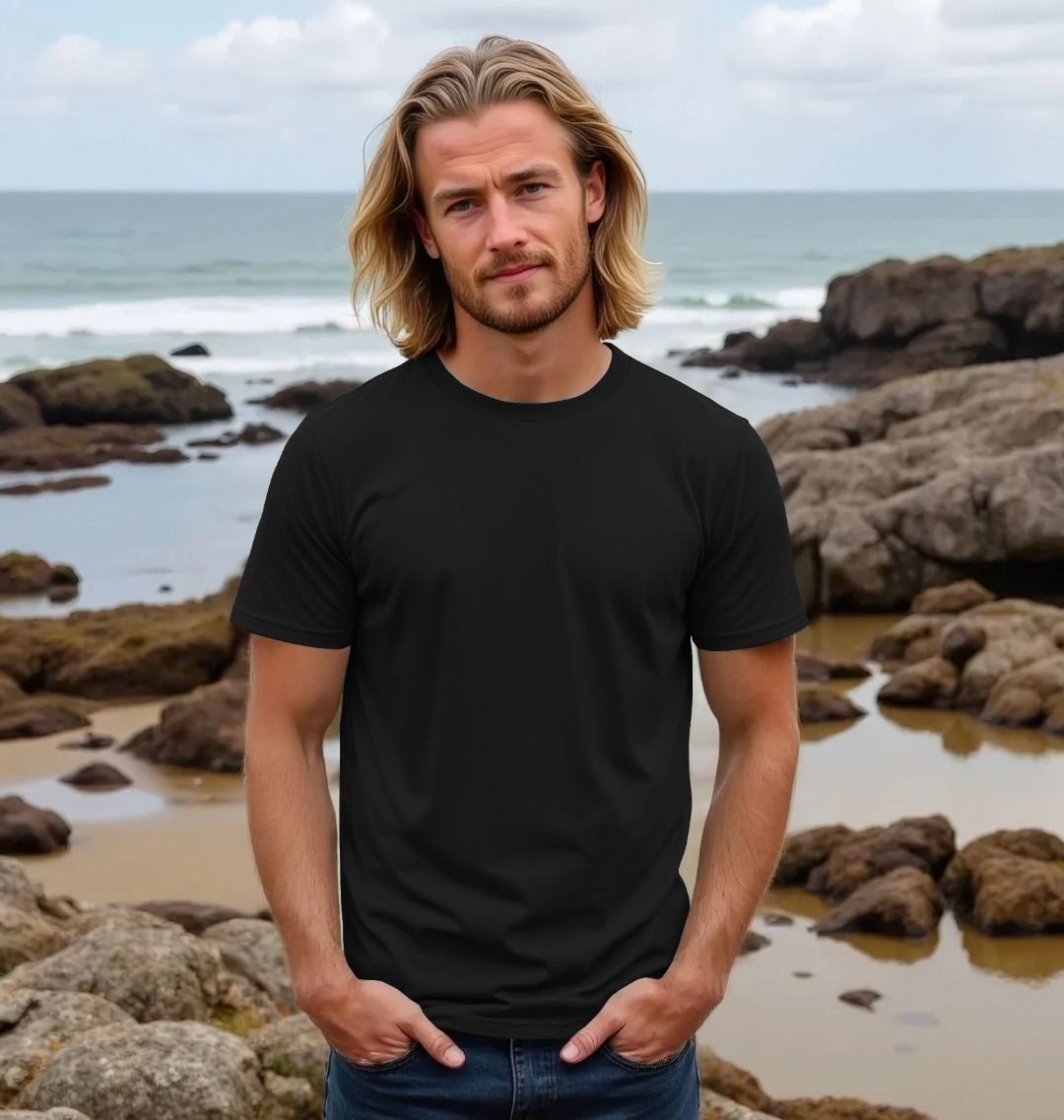 Man wearing a black t-shirt standing on a rocky beach with ocean in the background