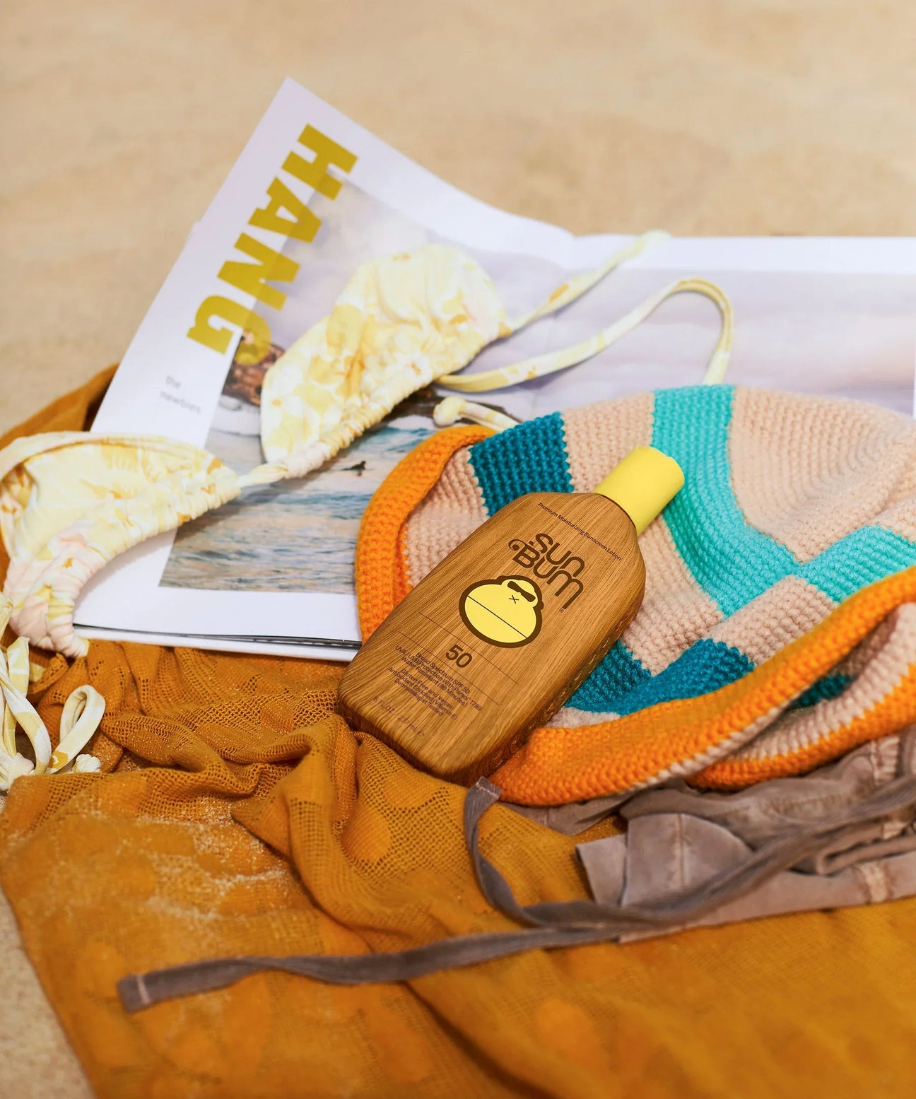 a close up of a beach scene with a towel, bikini top and a bottle of sun bum 50 spf reef safe sunscreen