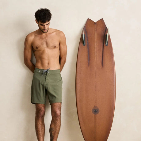 Man standing next to a wooden surfboard against a plain background