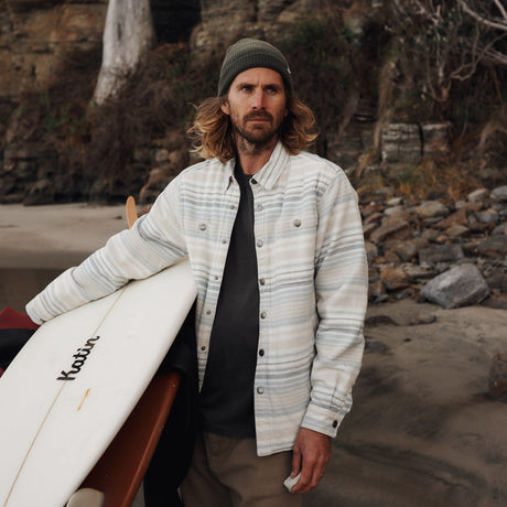 Man holding a surfboard on a rocky beach with cliffs in the background
