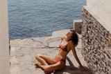 Woman in a bikini sitting by a stone wall with water in the background