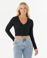 Woman wearing a rip curl black cropped cardigan and blue jeans on a white background
