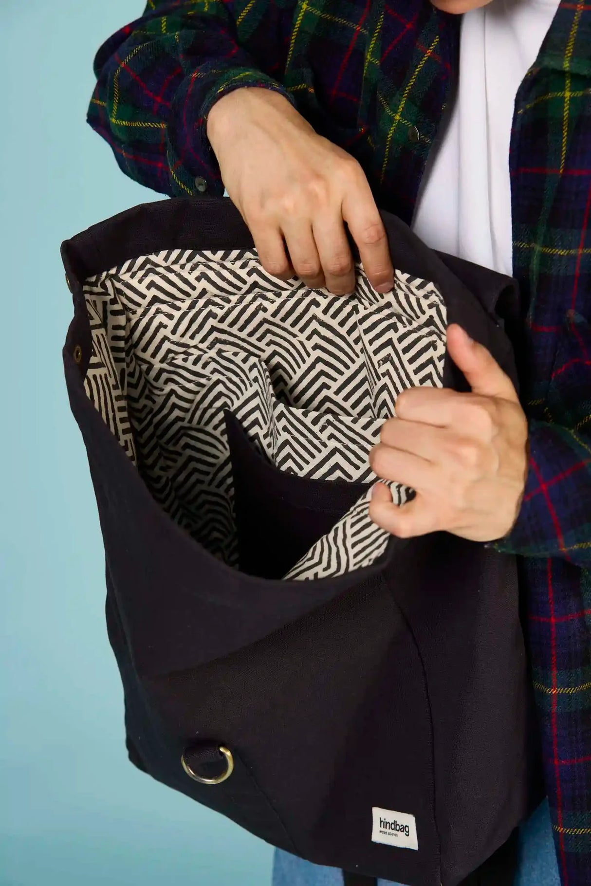 Person holding a waterproof black backpack from Hindbag with a patterned compartment against a blue background