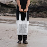 man holding white shopper tote bag with wave design