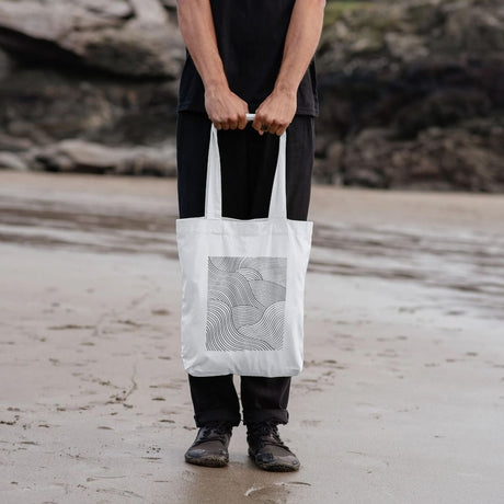 man holding white shopper tote bag with wave design